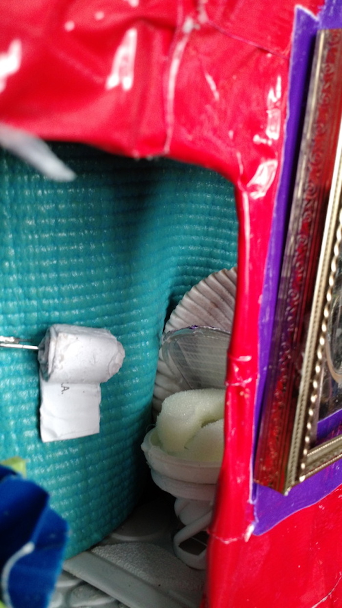 Photo of the sample mockup of Sessaris's apartment, removed from the shelving, seen from the back, This view looks in through the door and around the corner into a bathroom, which in this version contains a toilet with a lid made of a scallop shell.